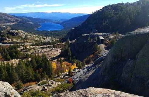 View from the top of a rocky hill looking at Lake Tahoe in the distance surrounded by mountains with green trees
