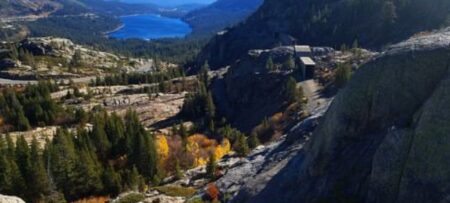 View from the top of a rocky hill looking at Lake Tahoe in the distance surrounded by mountains with green trees