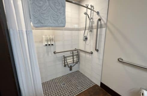 Large white tiled walk-in shower with silver hand rails and bench