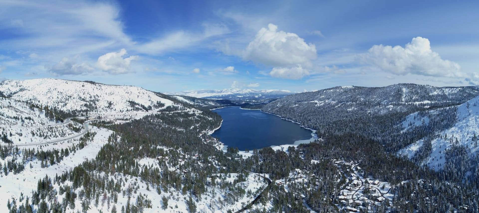 Aerial view of Lake Tahoe situated between two mountains covered with green trees and white snow